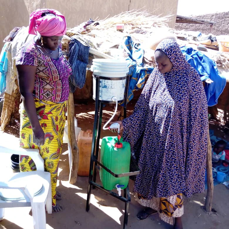 Frau in Afrika zapft Wasser aus Wasserfilteranlage von faircap