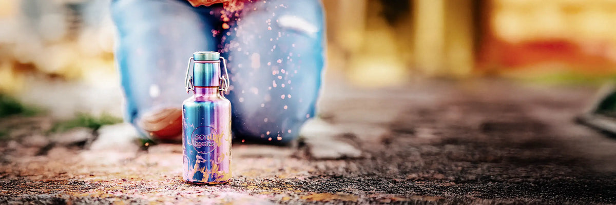 Trinkflasche aus Edelstahl im Regenbogen-Look auf Steinboden